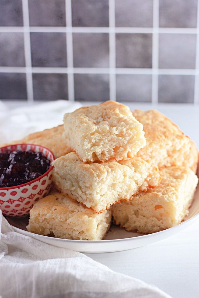 butter biscuits stacked on plate on table with grape jelly around it 