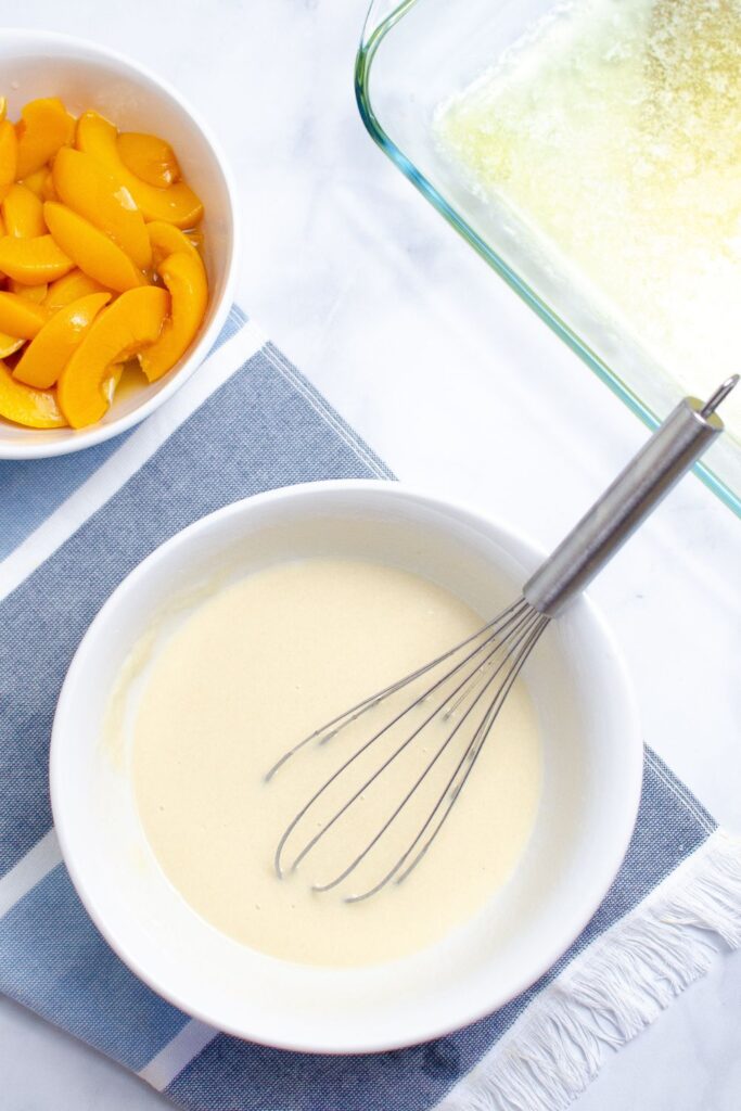 peach cobbler flour batter mixed up in a white bowl on table with a whisk in it
