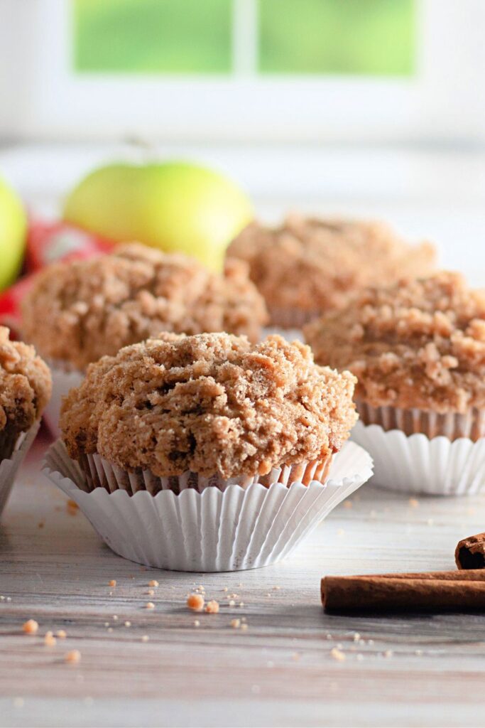 muffins on counter with cinnamon sticks and apples on table