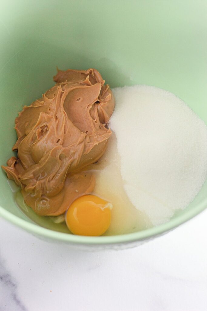 peanut butter, egg and sugar in a green mixing bowl 