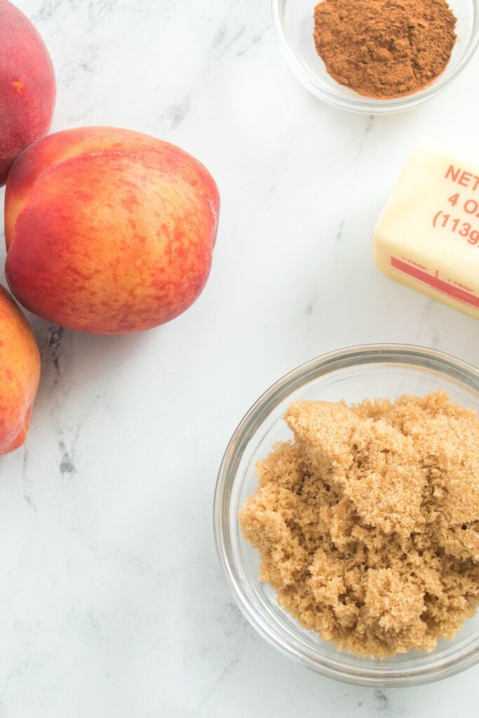 ingredients for Air Fryer Peaches on table. Peaches, bowl of cinnamon, bowl of brown sugar, and butter