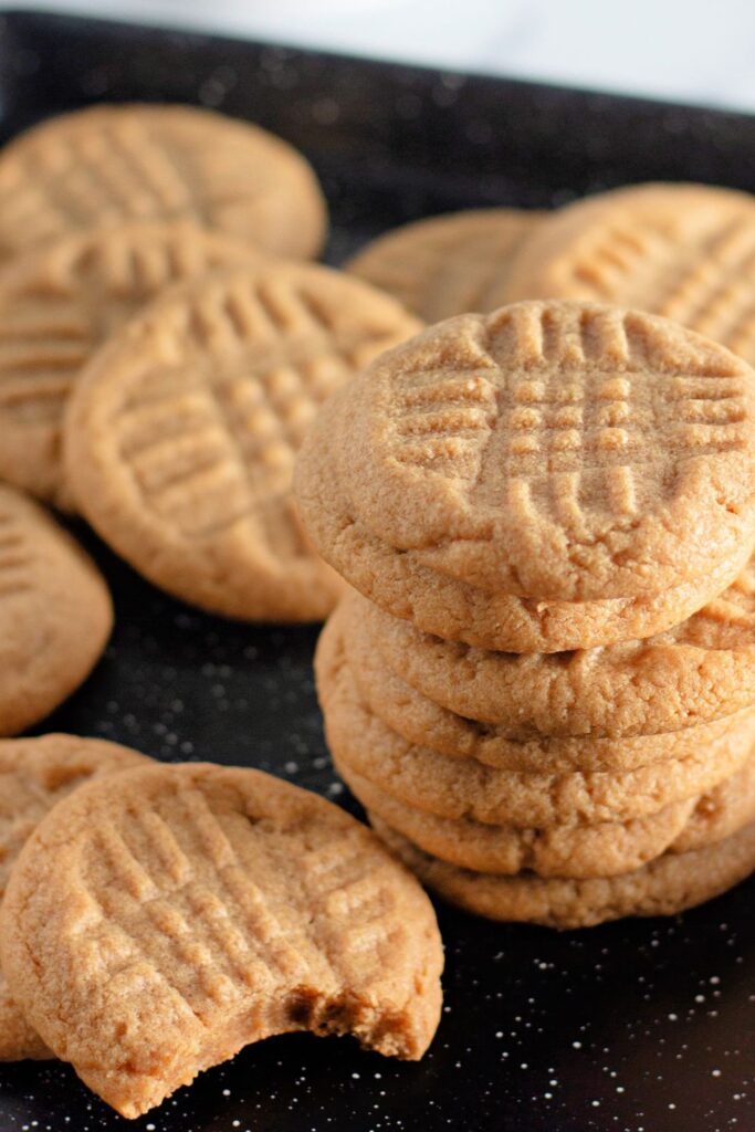 stacked peanut butter cookies on table with one cookie with a medium sized bite taken out of it 