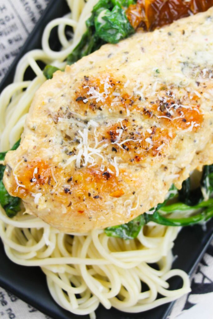 close up of seared chicken with parmesan cheese on top sitting on a plate on table