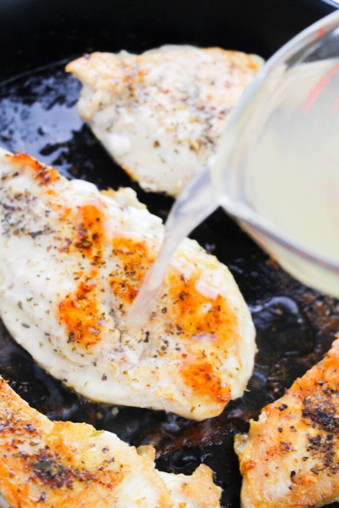 pouring broth over seared chicken that is in a cast iron skillet 