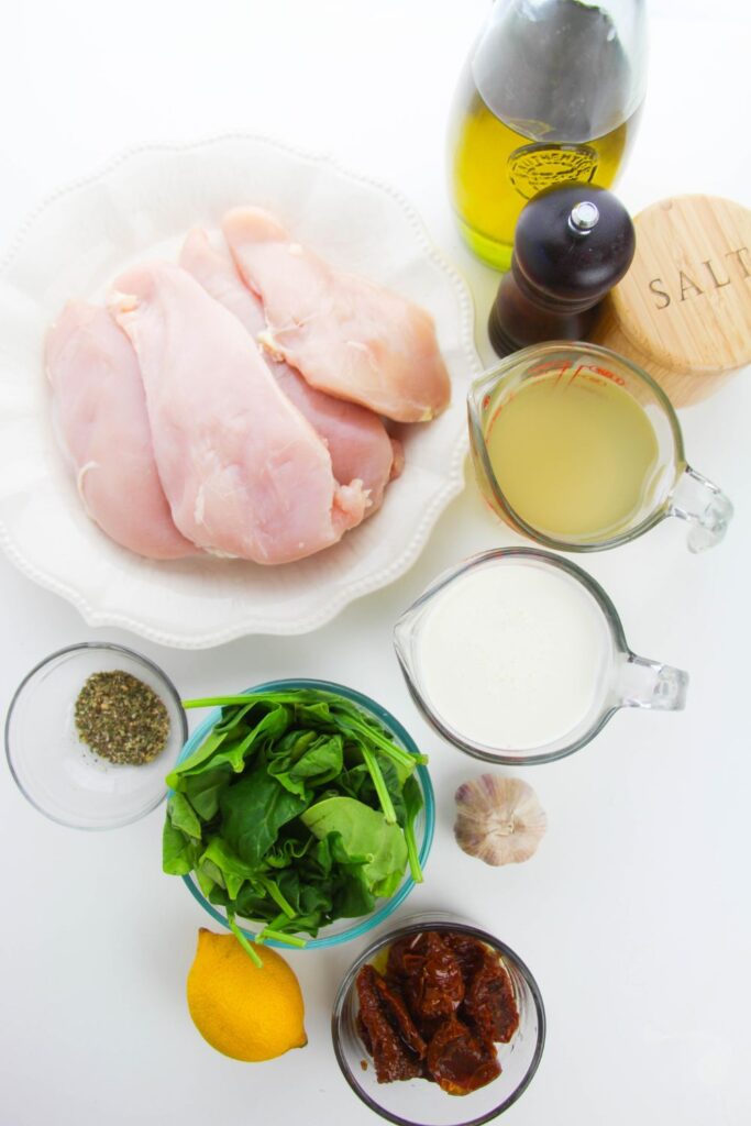 ingredients on table in single serve containers: boneless chicken, broht, heavy cream, spinach, seasonings, oil, salt, pepper, garlic 