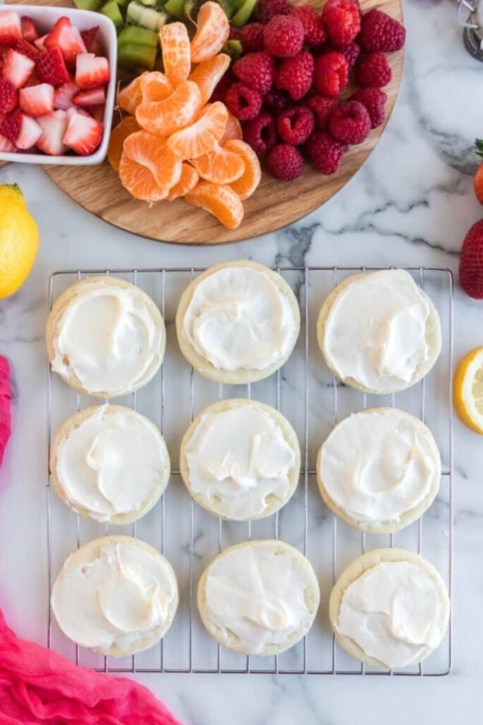 frosting sugar cookies on a cooling rack with fruit