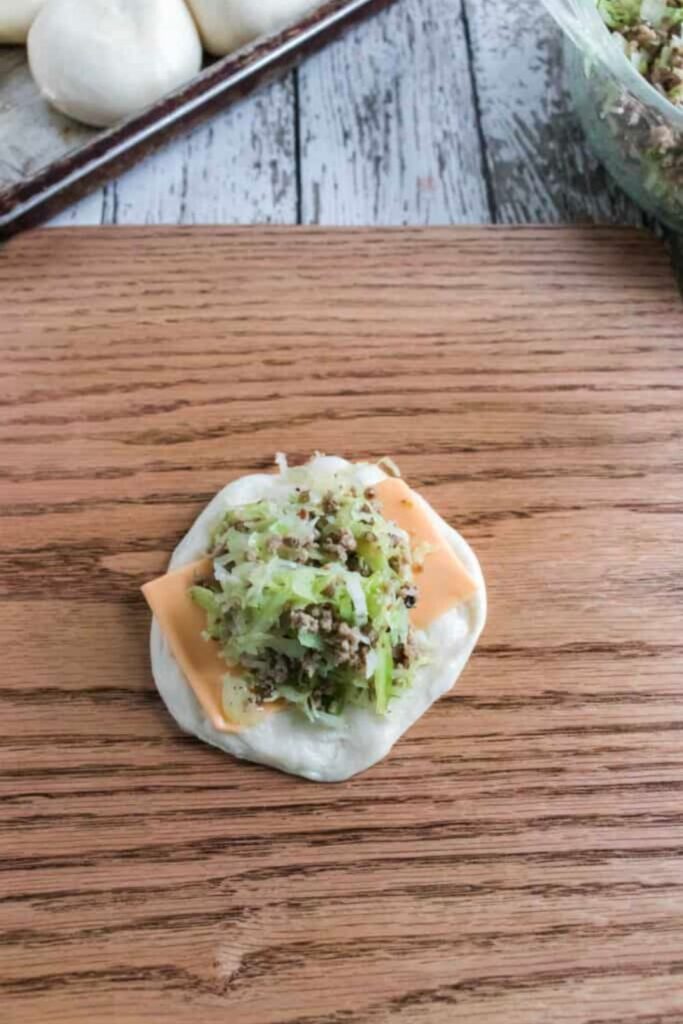 Raw bread dough with a slice of cheese and meet and cabbage filling in the center 