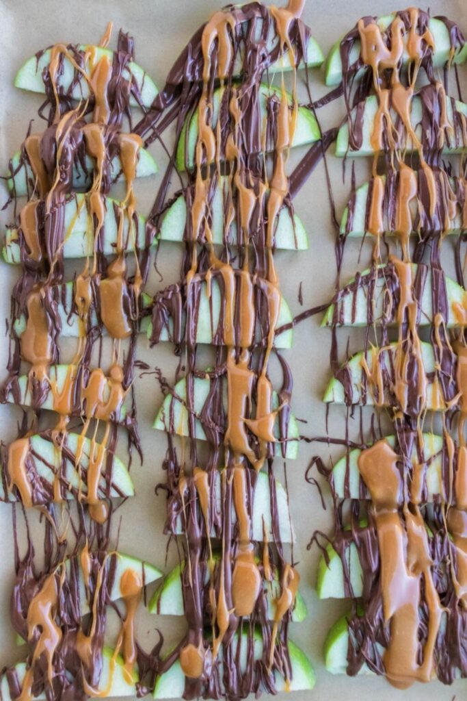 sliced apples on parchment paper drizzled with caramel and melted chocolate 