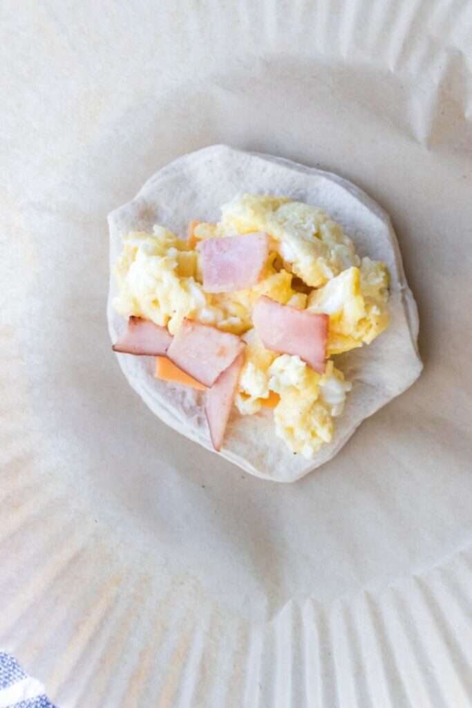 ham, egg and cheese on a biscuit sitting on parchment paper in an air fryer