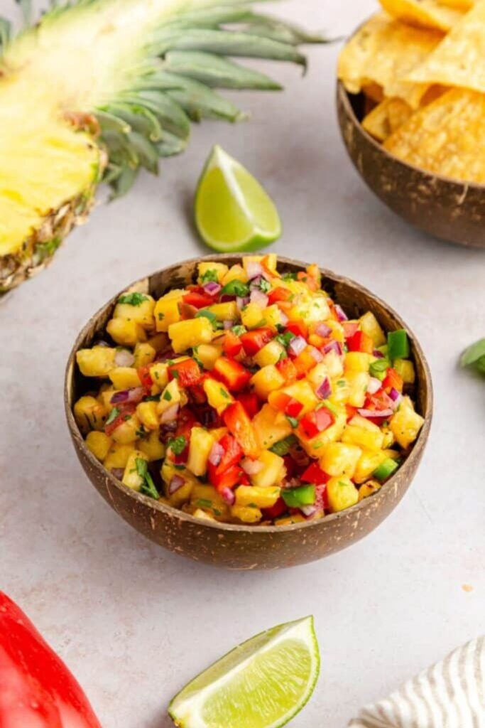 Pineapple Jalapeno Salsa in a bowl with chips to side and half a pineapple on table