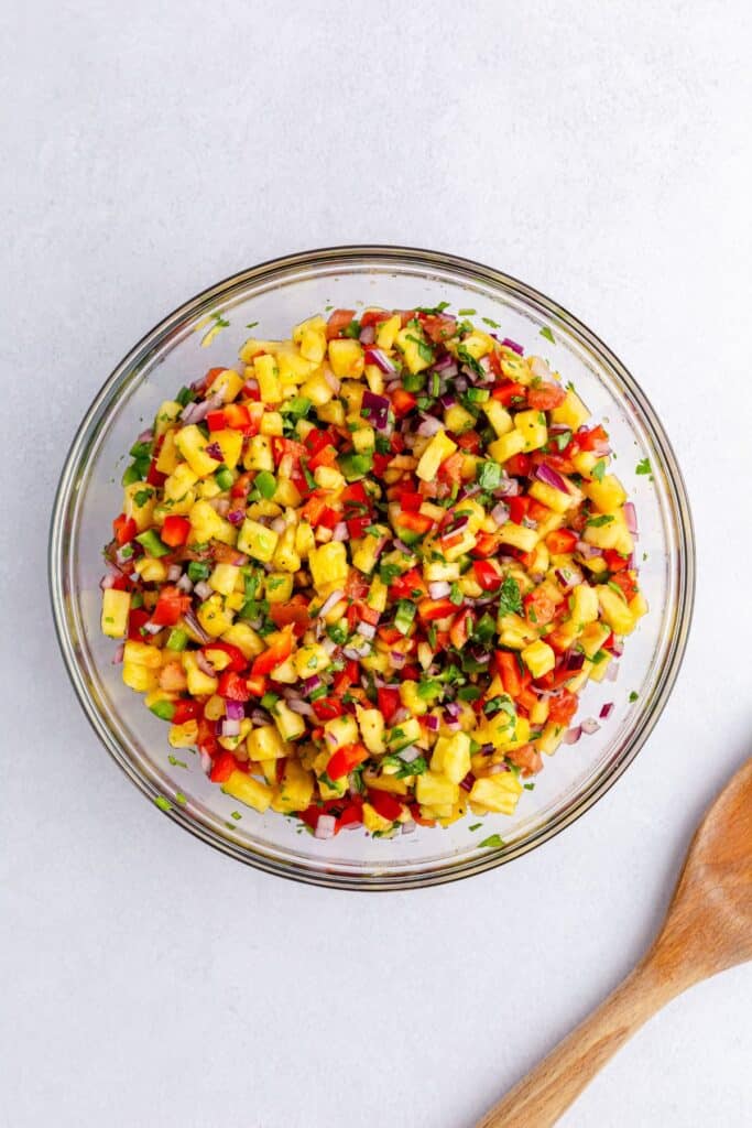 Pineapple Jalapeno Salsa mixed up in a bowl on table with a wooden spoon to side 