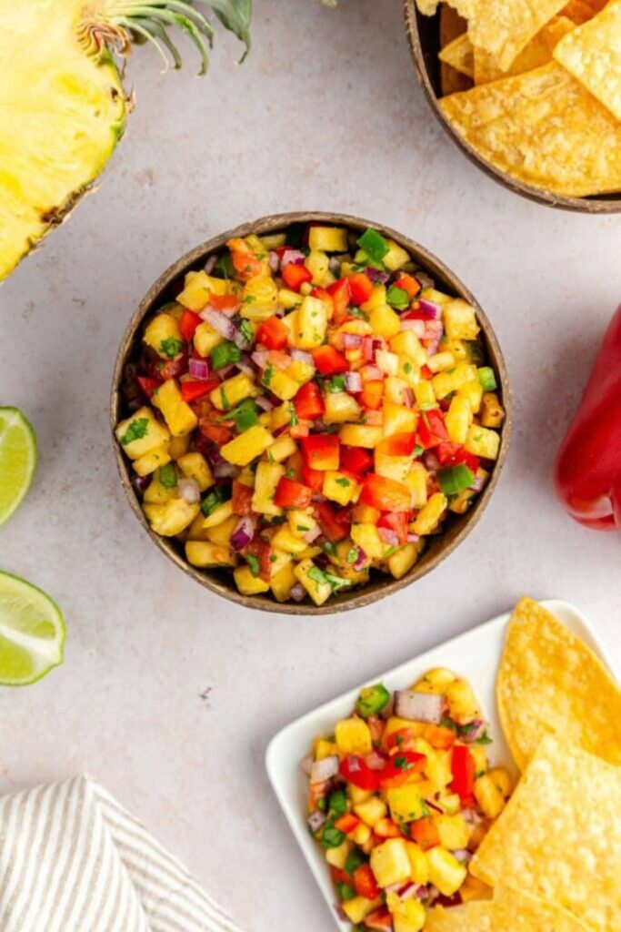 Pineapple Jalapeno Salsa in a bowl with a plate with more salsa on a plate with chips 