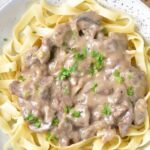 Beef Stroganoff on a plate with noodles under it and the stroganoff is topped with parsley
