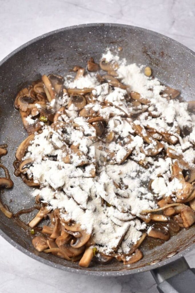 mushrooms in pan with a flour mixture poured over top for making the sauce for beef stroganoff