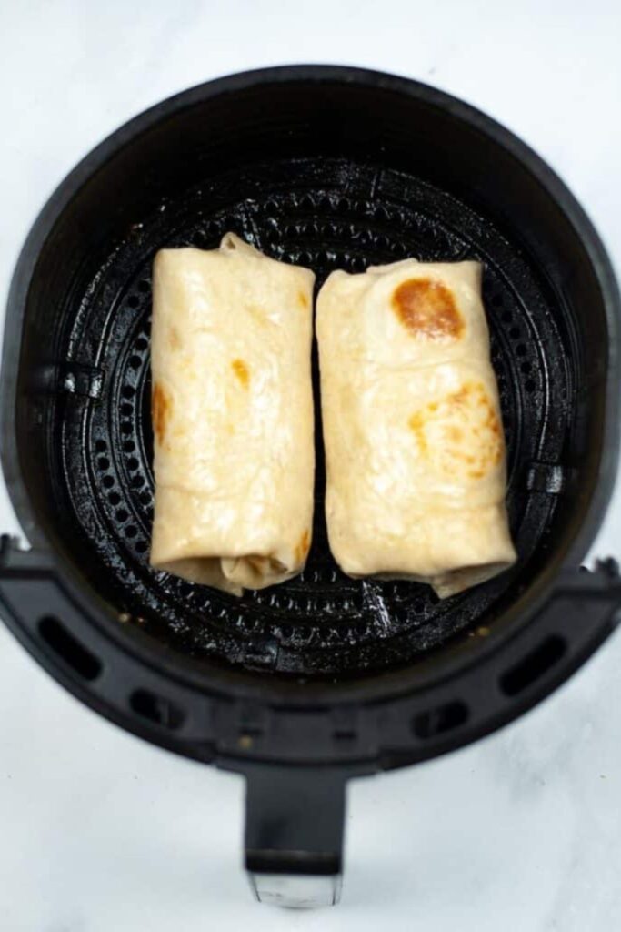 Breakfast Chimichangas in an air fryer basket sprayed with oil 