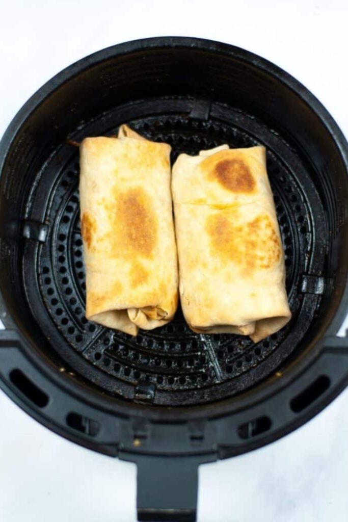 Breakfast Chimichangas in an air fryer basket cooked up till crispy 