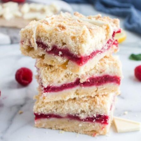 Raspberry Crumble Bars stacked on top of one another on a marble counter with some fresh berries around the table