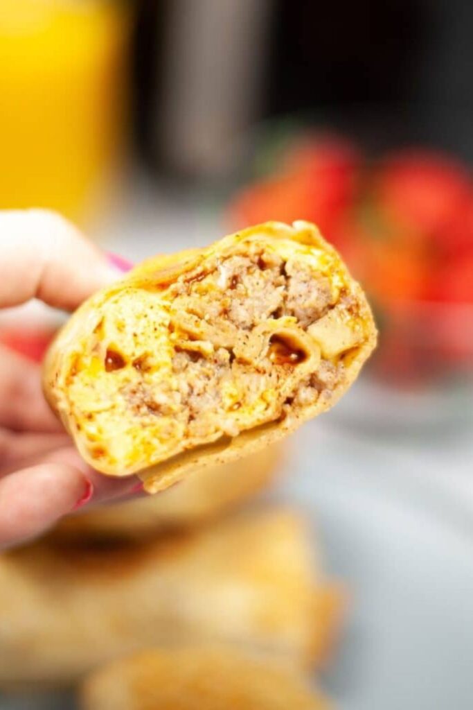 Breakfast Chimichanga in a persons hand with some bites taken out of it 