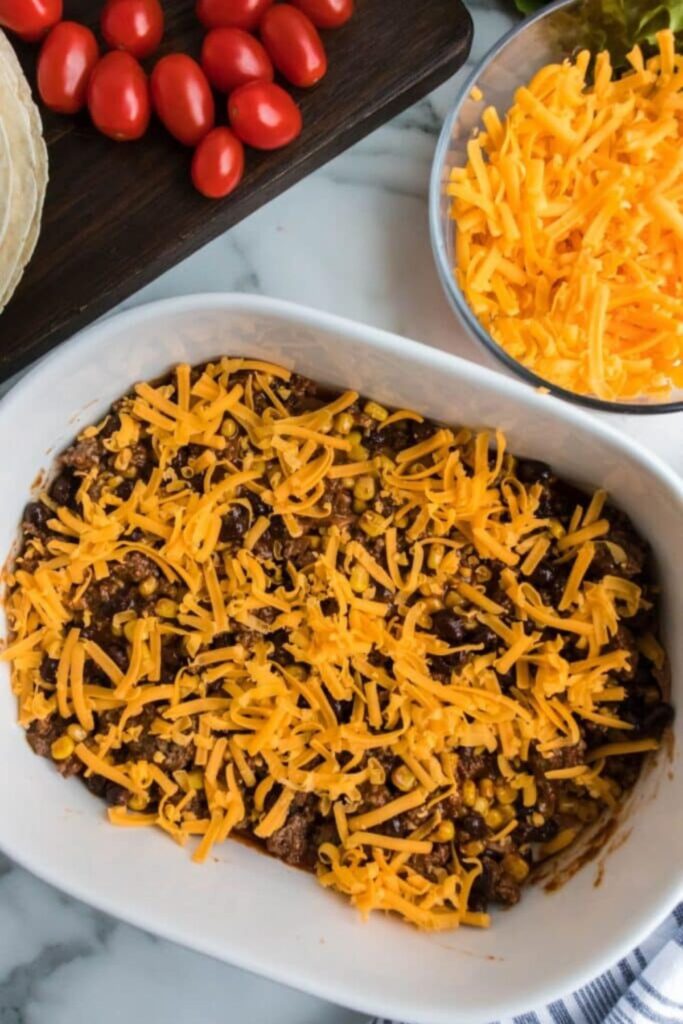 ground beef and cheese spread in a round casserole pan on table with a bowl of cheese to the side