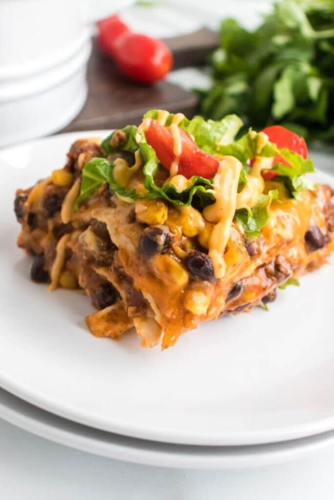 Layered Beef Enchilada Casserole on a plate topped with lettuce and tomatoes
