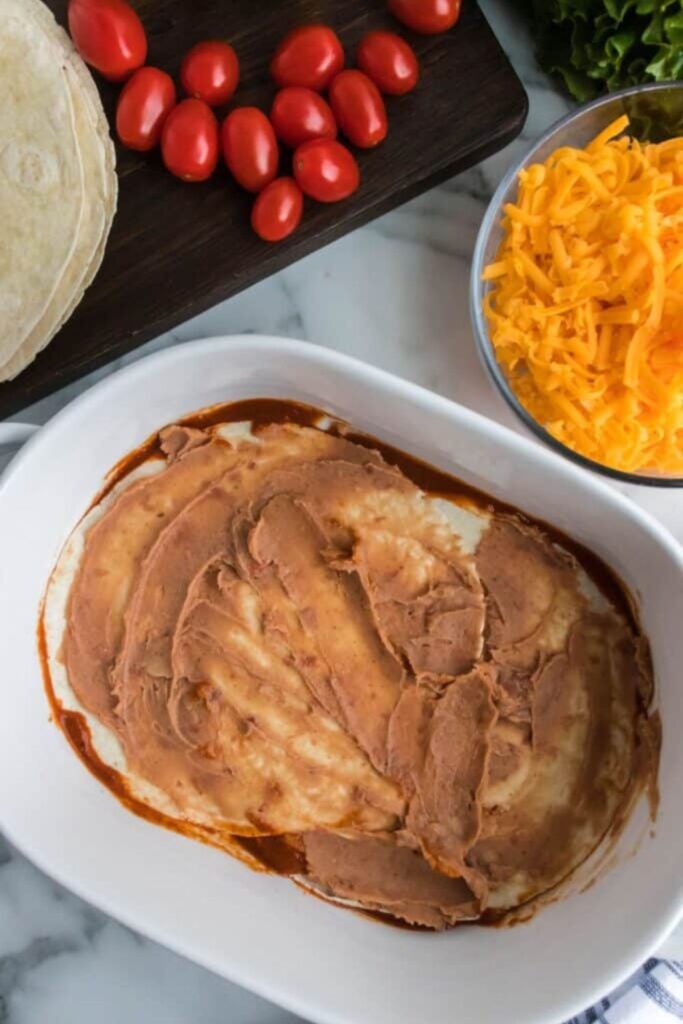 tortillas spread in pan with refried beans on top