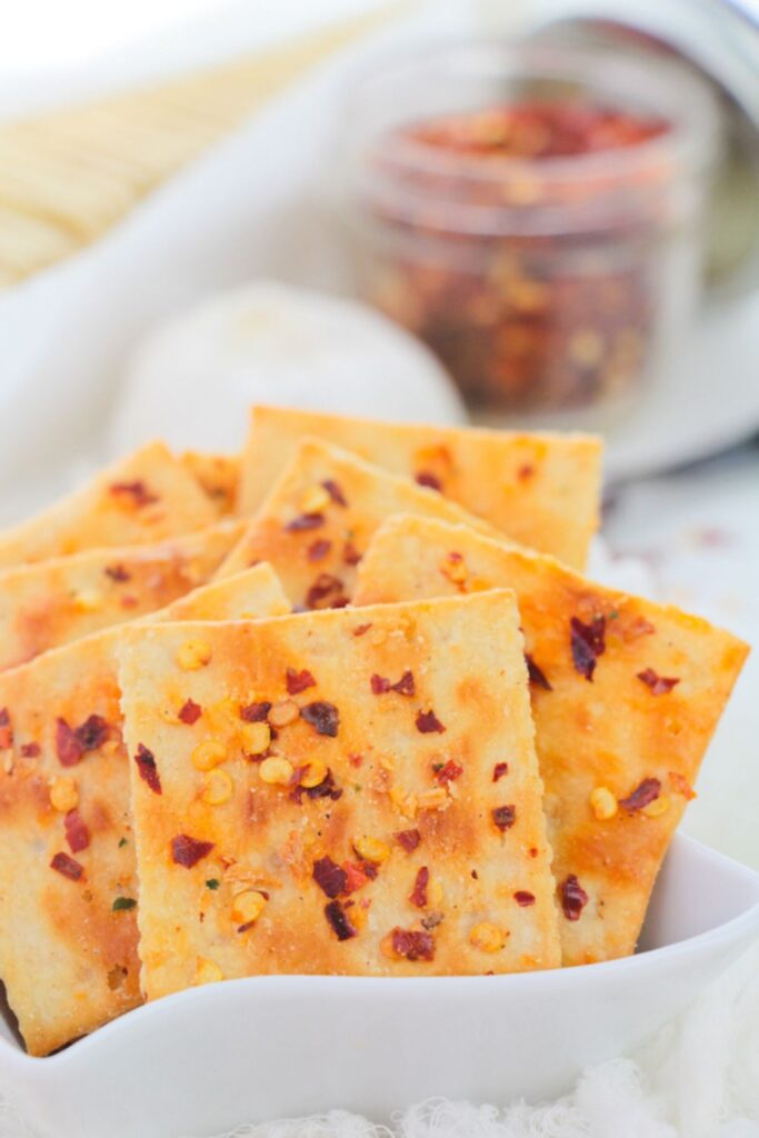 a bowl of spicy crackers on table with a jar to side full of red pepper flakes