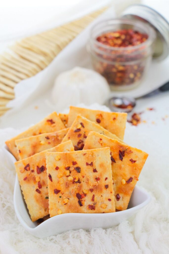 spicy ranch crackers in a bowl with red pepper flakes in a jar on table behind it