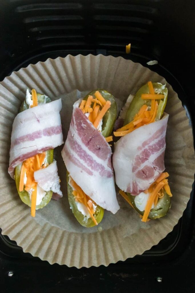 Air Fryer Bacon Wrapped Pickles in a parchment paper lined air fryer basket to be air fried