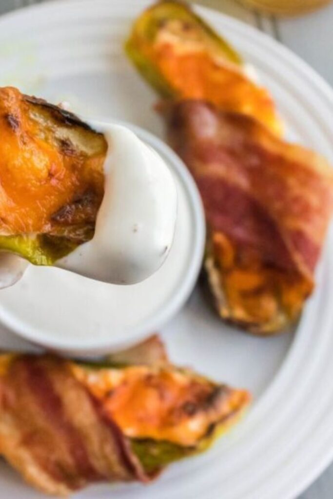 plate full of bacon wrapped pickles with one being dipped into a sauce