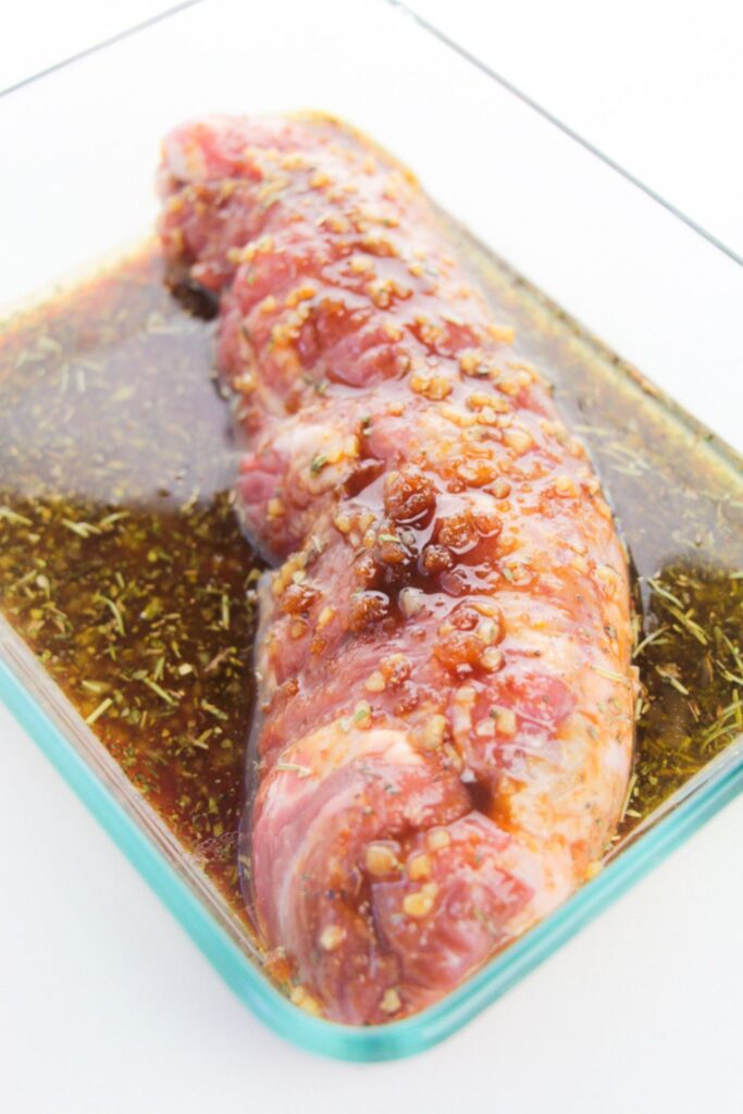 a glass bowl with a raw tenderloin that is being marinated in a sauce
