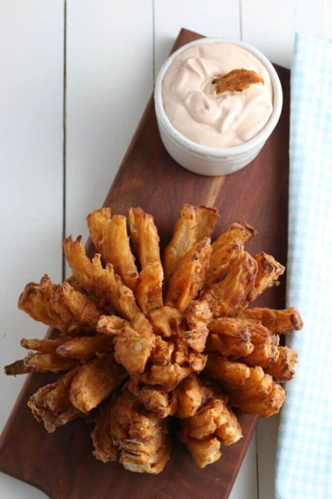 Air Fryer Blooming Onion on a wooden tray with a bowl of sauce to the side sitting on a white table