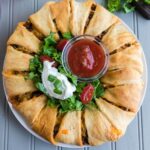 taco ring on table with sour cream and salsa in the center for dipping