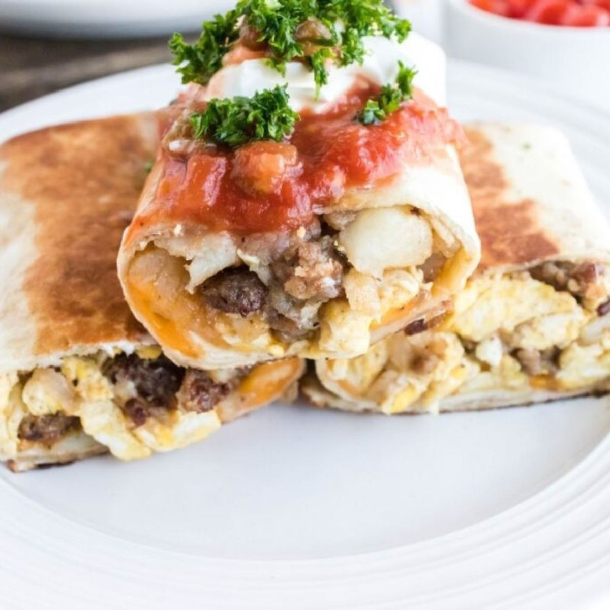 Blackstone Breakfast Burritos placed on a plate topped with sour cream and salsa