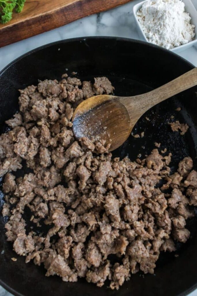 sausage cooked in a skillet with wooden spoon