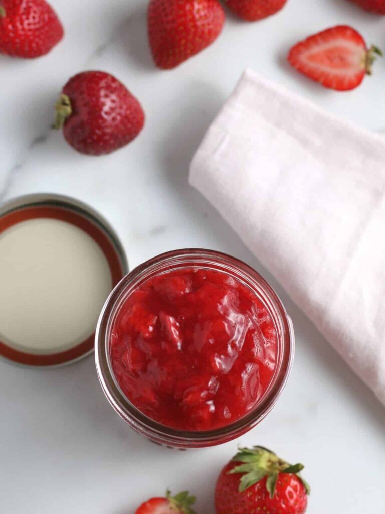 Strawberry sauce recipe in mason jar with fresh strawberries to the side on the table