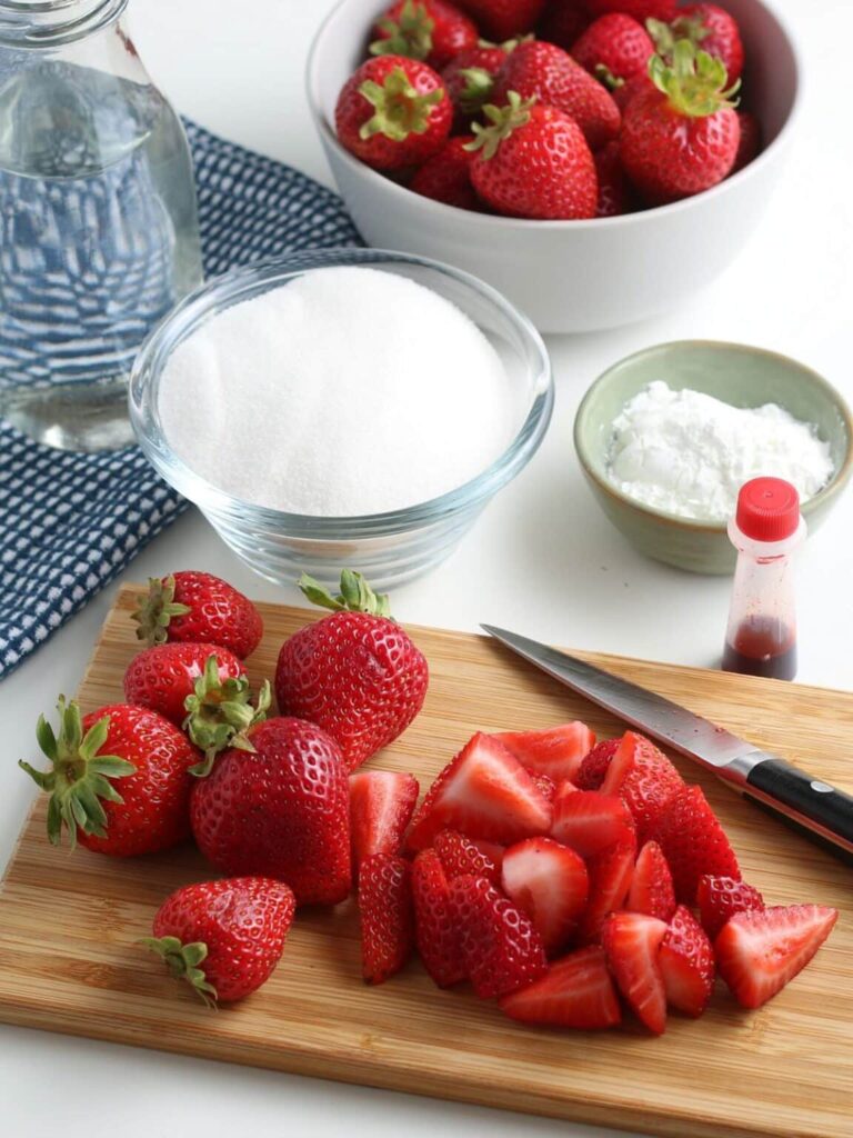 strawberries sliced up on a cutting board with sugar in the background and a bowl of sugar